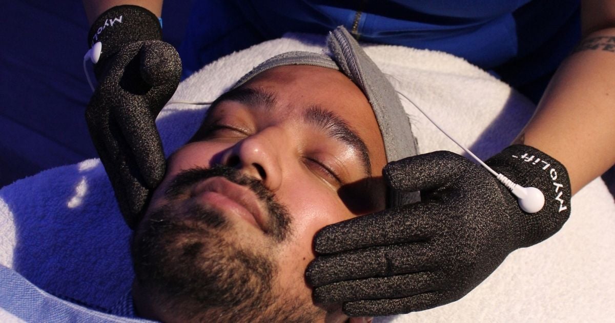 Esthetician using microcurrent gloves on a client's cheek and jawline at Nios Skin Lab